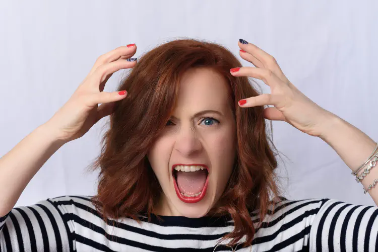 A picture of a woman from the shoulders up, yelling in frustration with her hands beside her head.